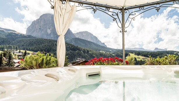 A hot tub with a mountain view, surrounded by greenery and red flowers. - Romantic & Family Hotel Gardenia (Selva di Val Gardena)