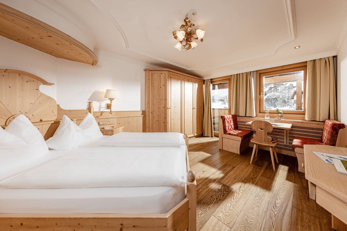 A hotel room with a wooden bed, a desk, a chair, and a window with curtains.