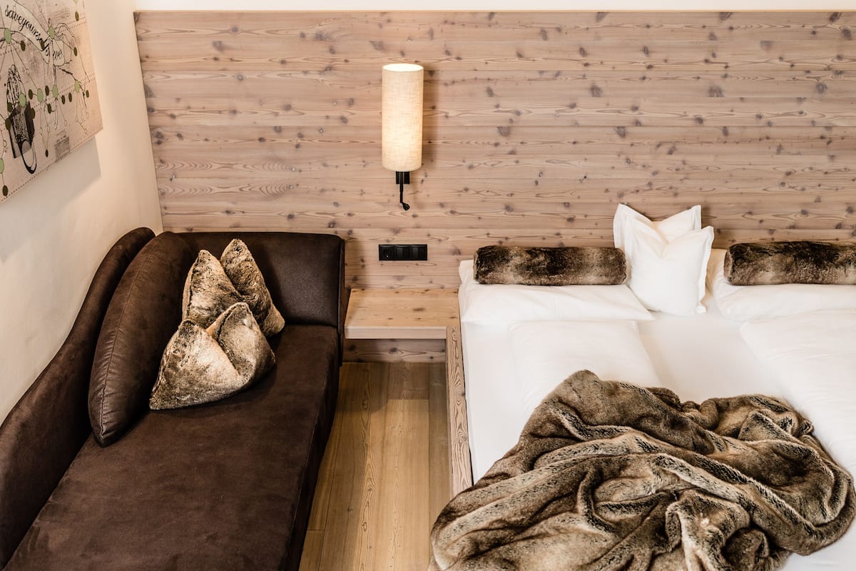 Ein Hotelzimmer mit einem Holz-Kopfteil, einem braunen Sofa mit Überwurfdecke und einem Bett mit weißen Bettwäsche und einer gemusterten Decke.
