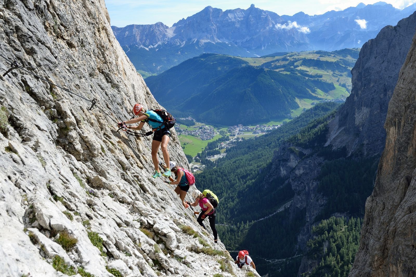 A group of hikers on a steep mountain path with a valley and distant mountains in the background.