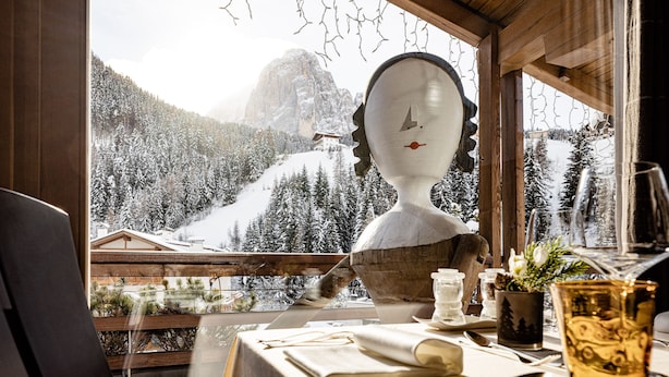 Une table à manger avec des couverts, un verre et une vue sur un paysage montagneux enneigé, visible à travers une fenêtre.