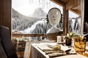 Een eettafel met bestek, een glas en uitzicht op een besneeuwd berglandschap door een raam.