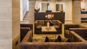 Un hall d’hôtel avec un comptoir d’accueil, des canapés en cuir, une table basse et un escalier en arrière-plan.