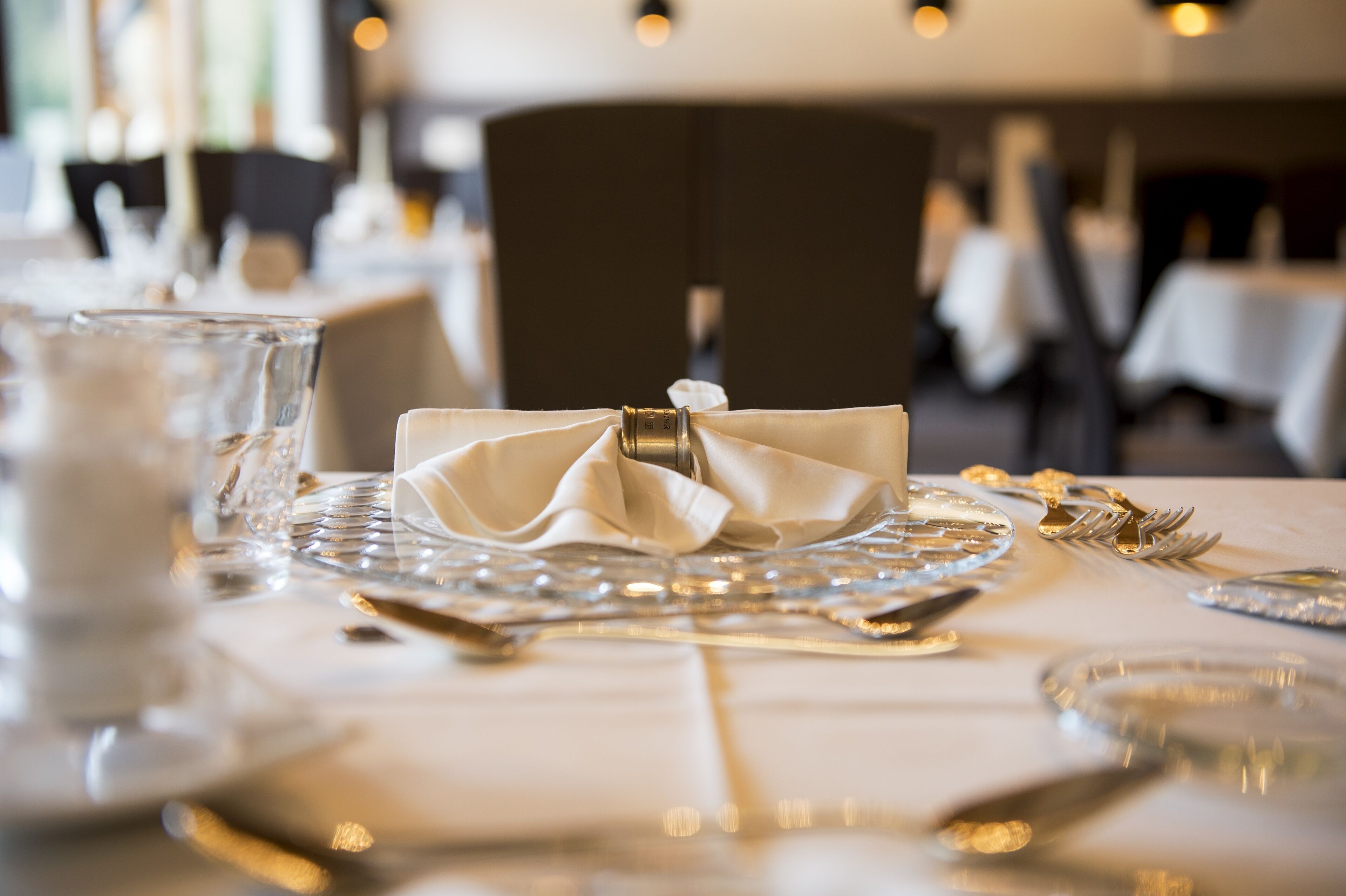 Une table à manger dressée avec une serviette pliée, de la verrerie transparente et des couverts.