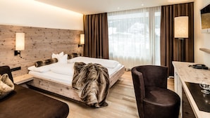 Une chambre d’hôtel moderne avec une tête de lit en bois, un lit recouvert de draps blancs, un fauteuil moelleux, un bureau avec une lampe et une grande fenêtre avec des rideaux.