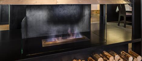 A modern fireplace with a metal hood, logs stored below, and a visible fire burning inside.