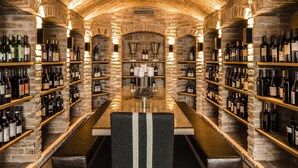 Una bodega con paredes de piedra, estantes de madera y una mesa central con sillas.