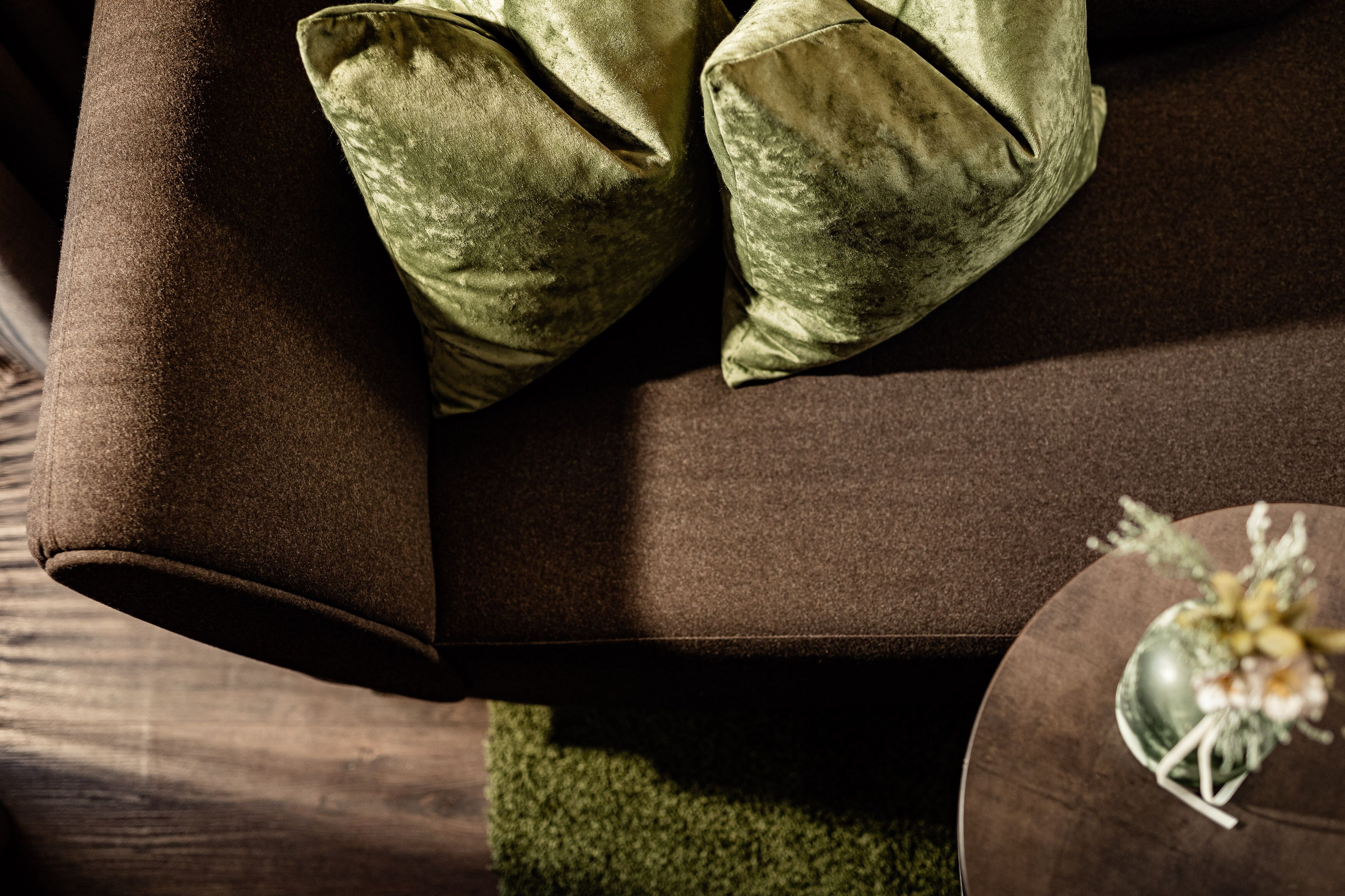 Un canapé marron avec des coussins verts et une petite table sur laquelle est posé un objet décoratif.