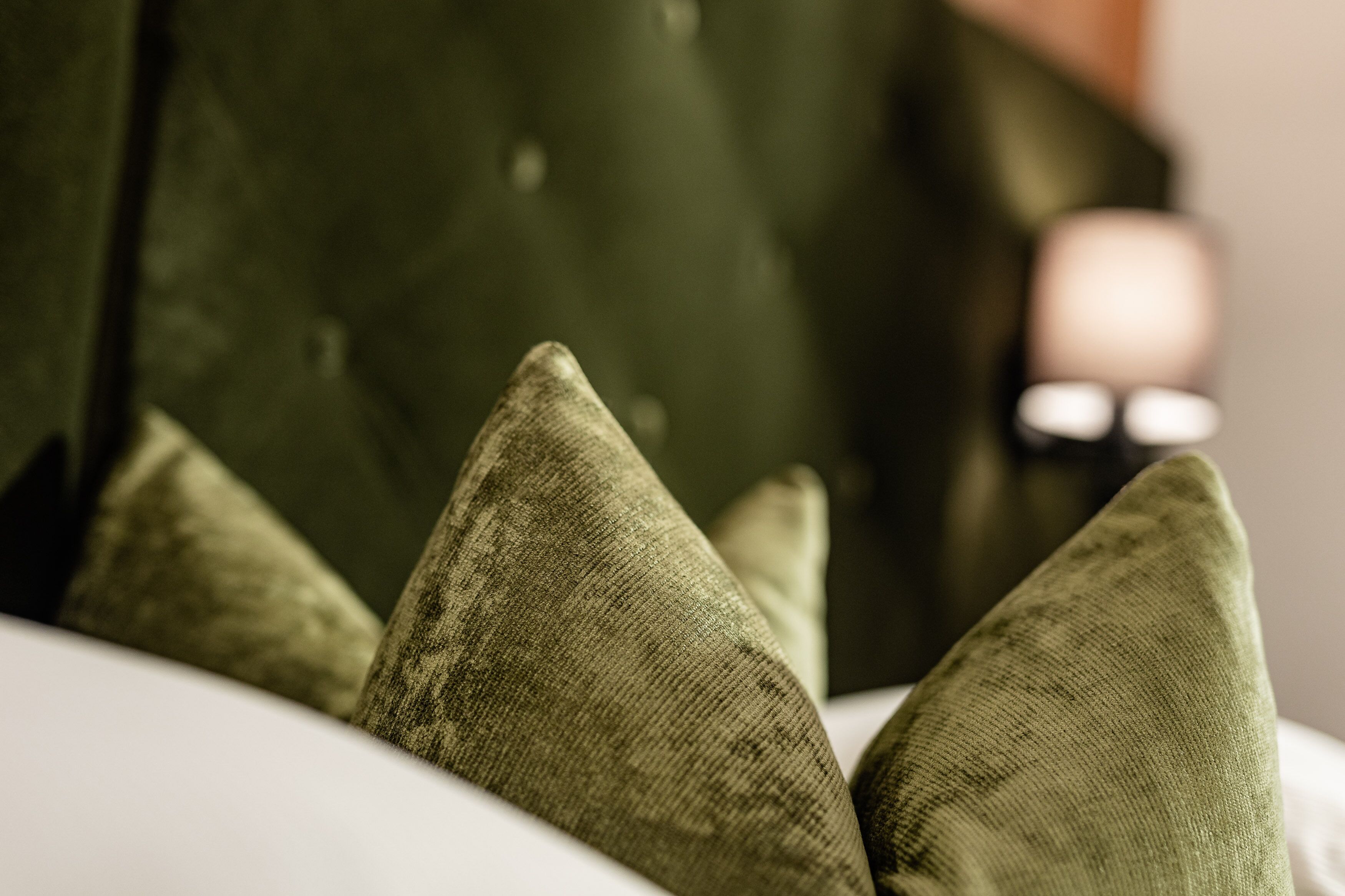 Un gros plan d’un lit avec des oreillers verts et une tête de lit sombre.