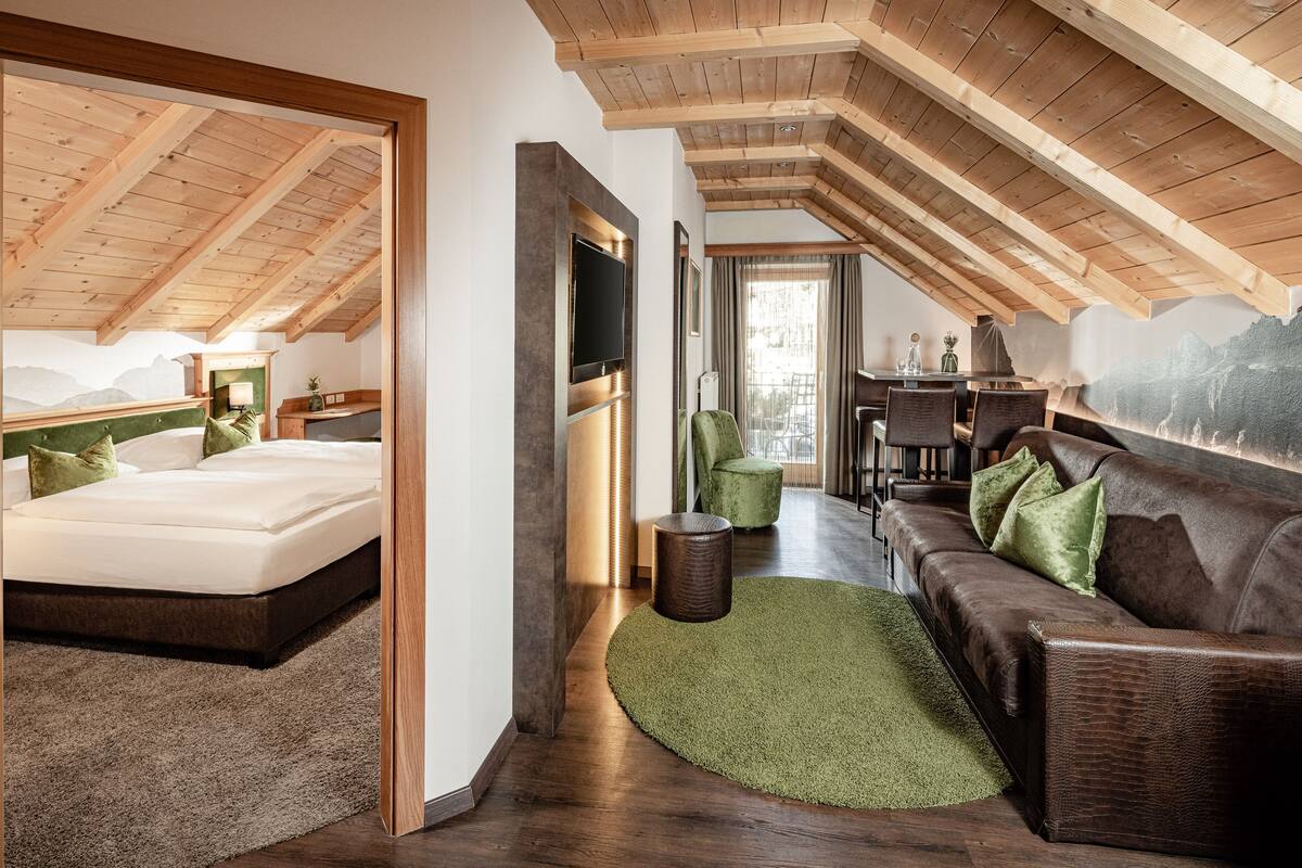 A modern bedroom with a large bed, a green rug, a brown leather sofa, and a wooden ceiling.