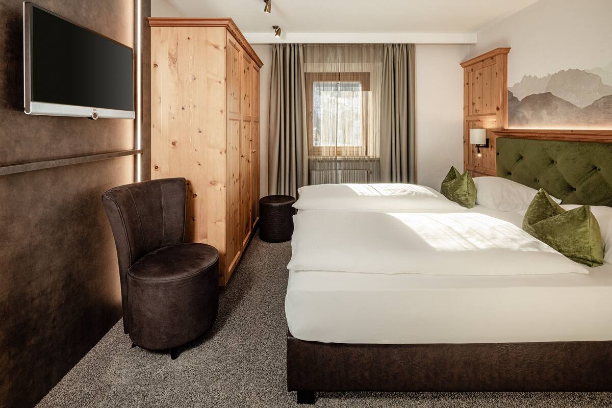 A hotel room with a large bed, a chair, a wardrobe, and a television.