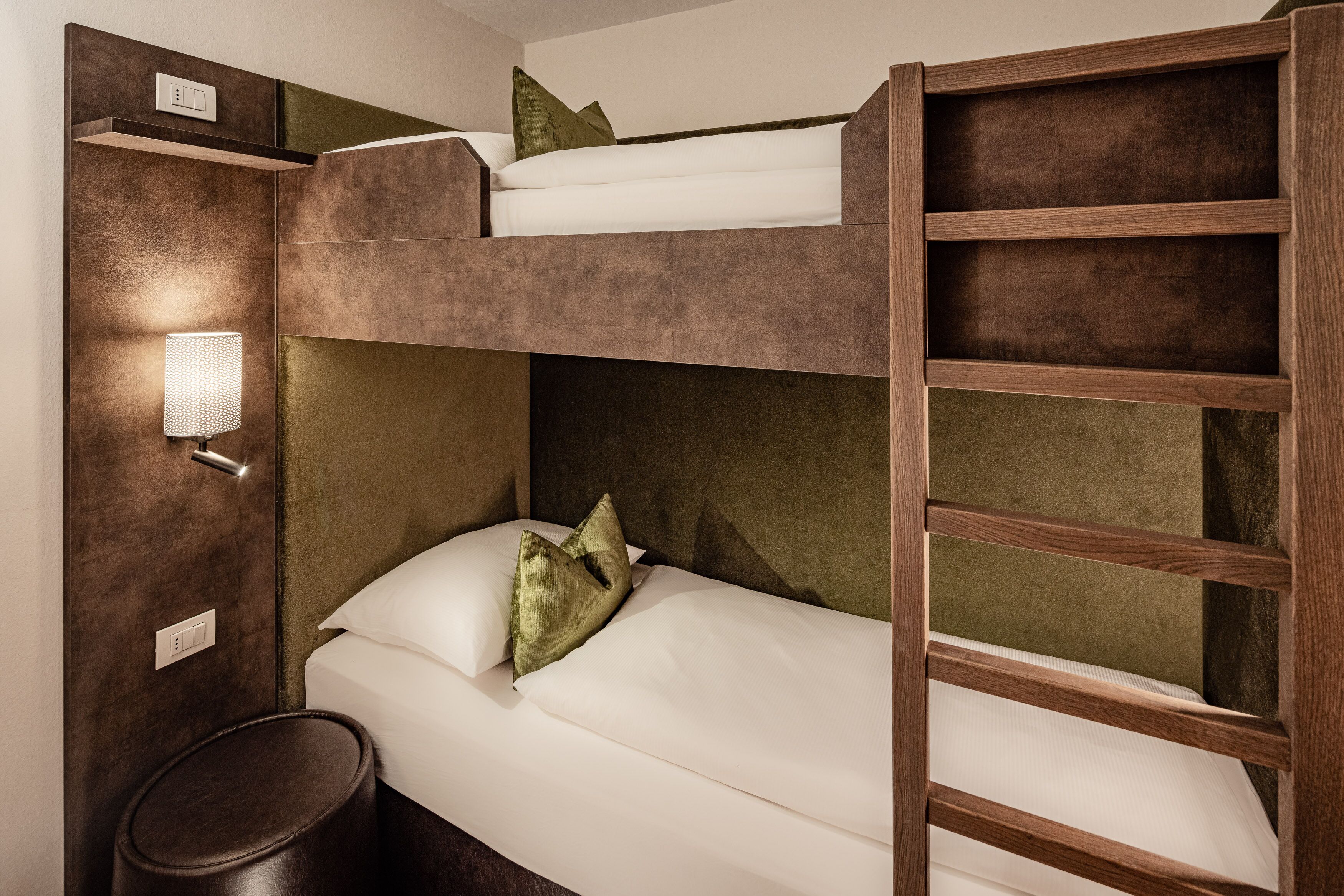 Een stapelbed met houten frame, een klein nachtkastje en een wandlamp.