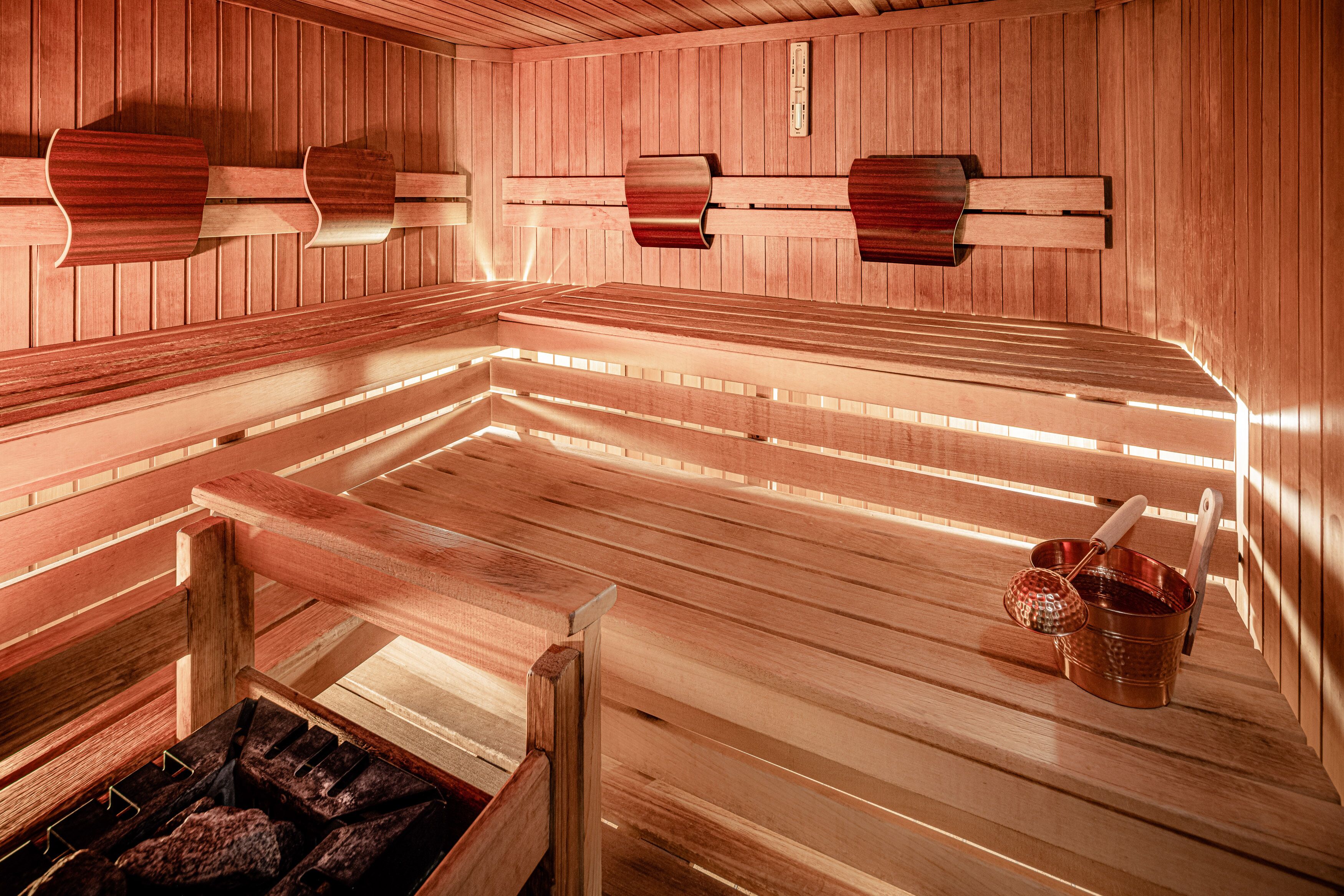 Un sauna avec des bancs en bois, un mur en bois muni d’un porte-serviettes et un seau avec une brosse.