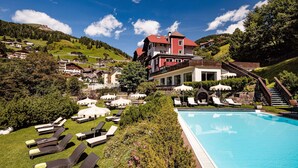 A resort with a swimming pool, sun loungers, and a view of the surrounding hills. - Boutique & Fashion Hotel Maciaconi (Selva di Val Gardena)