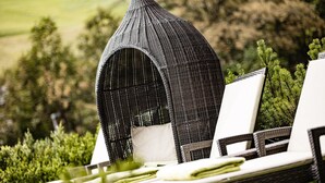 Outdoor wicker lounge chairs with white cushions and a unique black woven structure in the background. - Boutique & Fashion Hotel Maciaconi (Selva di Val Gardena)