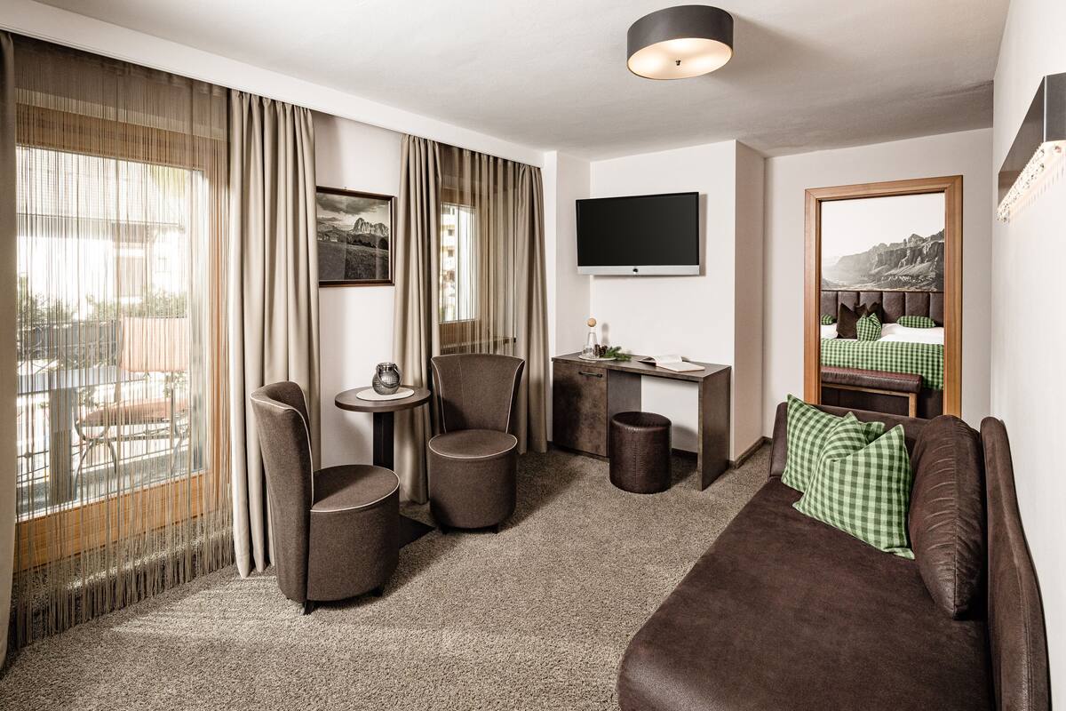 A hotel room with a sofa, two armchairs, a small table, a TV, and a view of the outdoors.