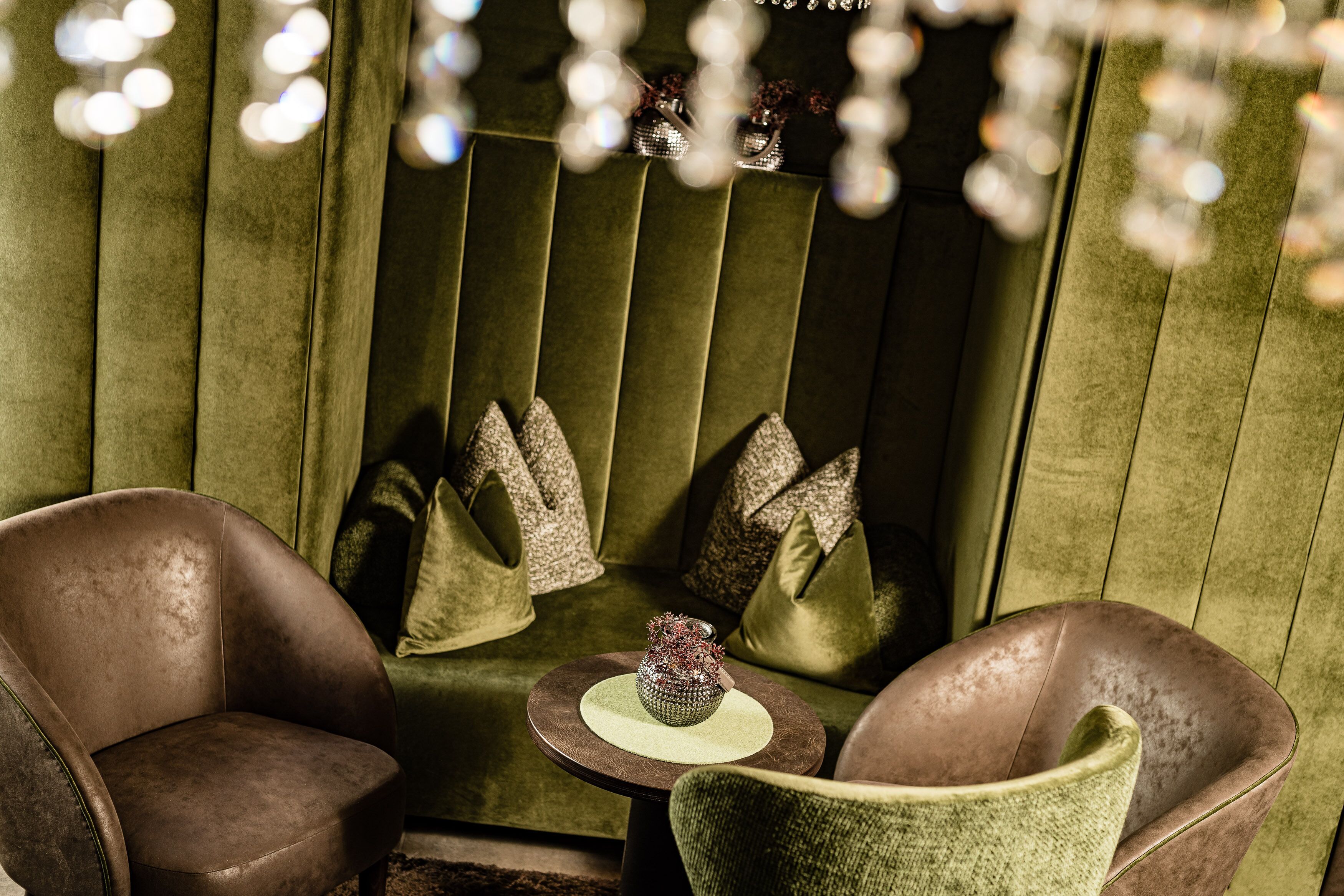 A cozy seating area with a green upholstered sofa, two leather armchairs, and a small round table with a decorative vase.