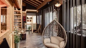 A modern interior with a hanging chair, wooden shelves, and a view of the outdoors. - Boutique & Fashion Hotel Maciaconi (Selva di Val Gardena)