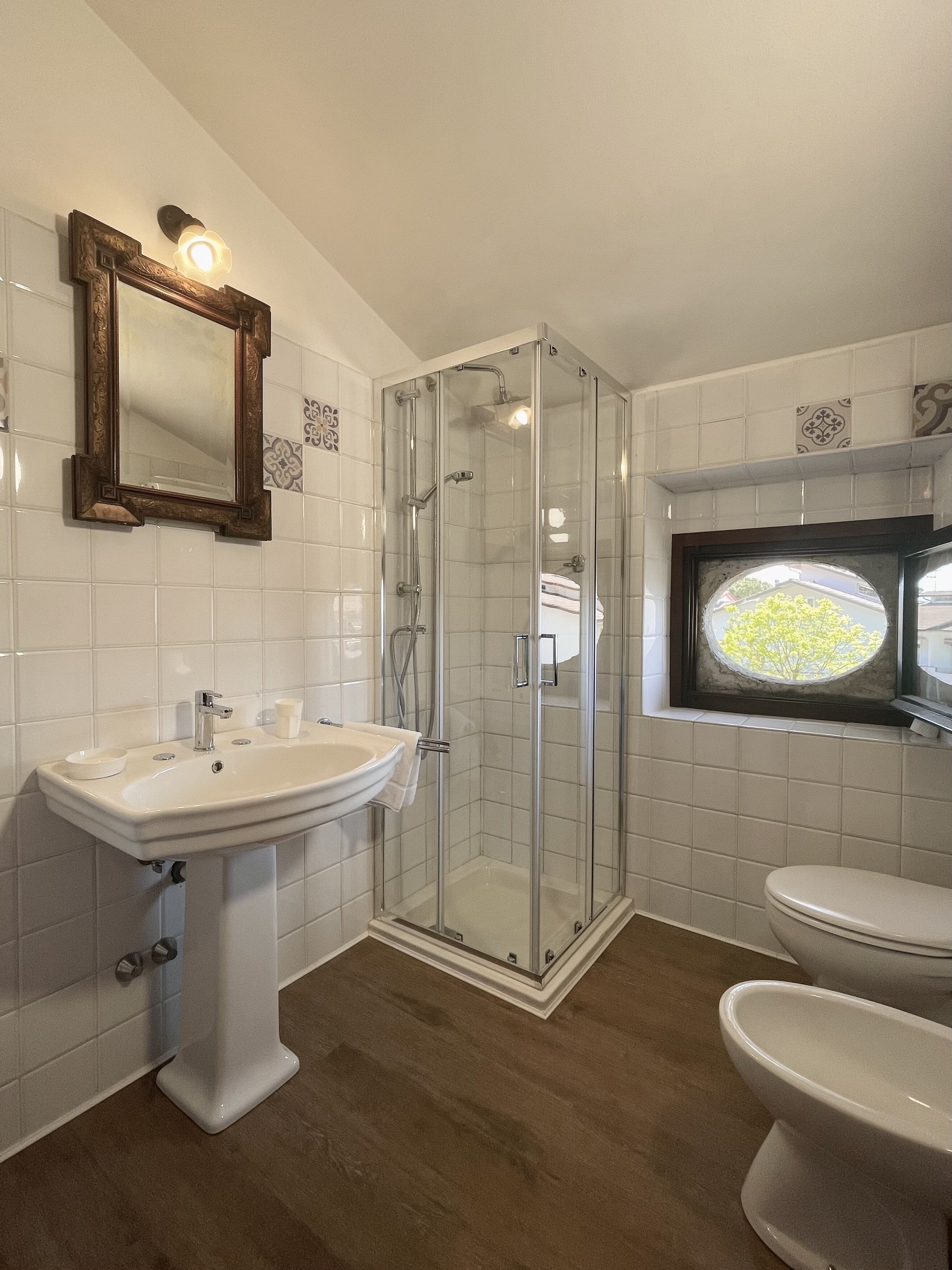 Un baño con ducha de vidrio, lavamanos pedestal y retrete.