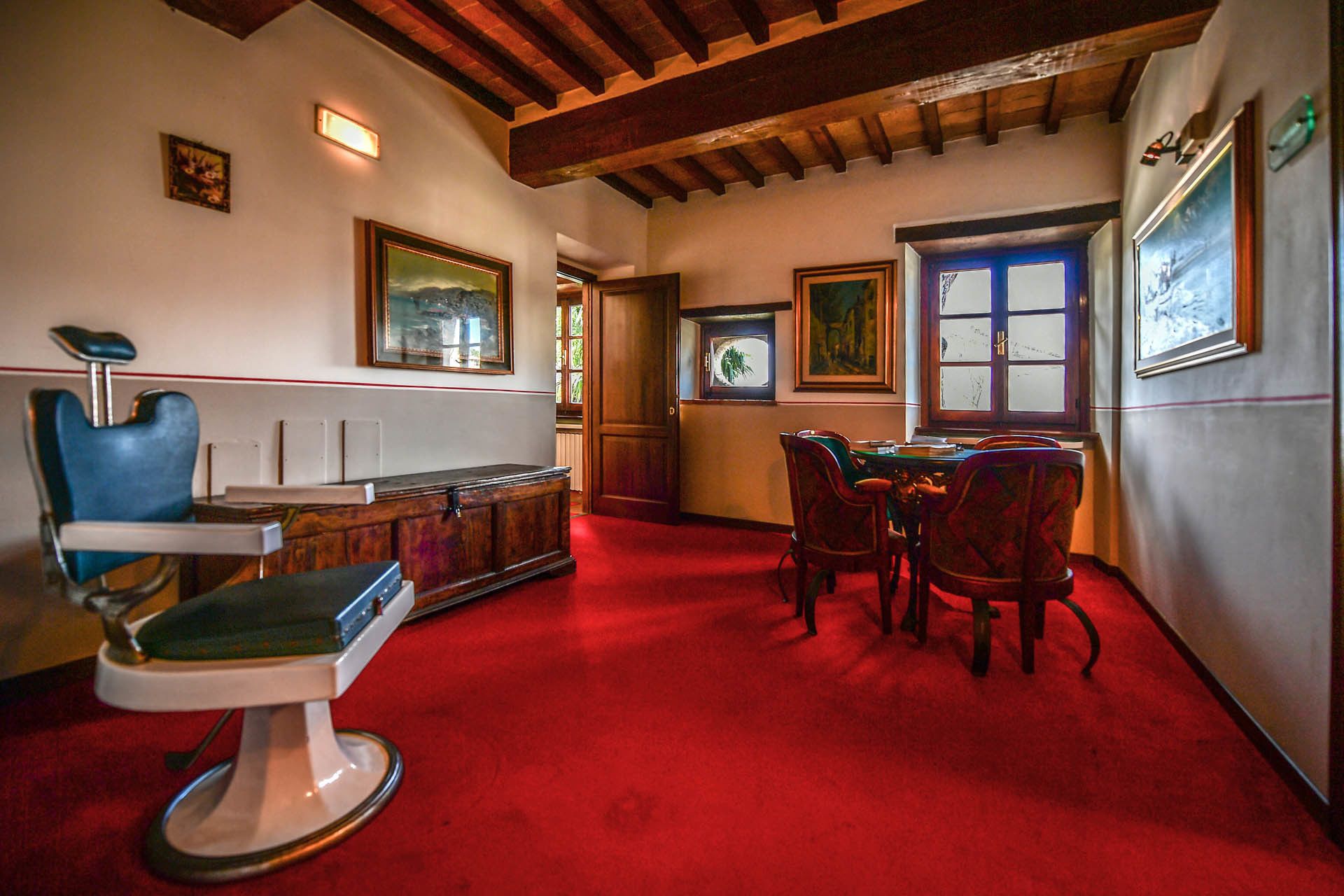Una habitación con alfombra roja, una silla azul, un armario de madera y una mesa de comedor con sillas.