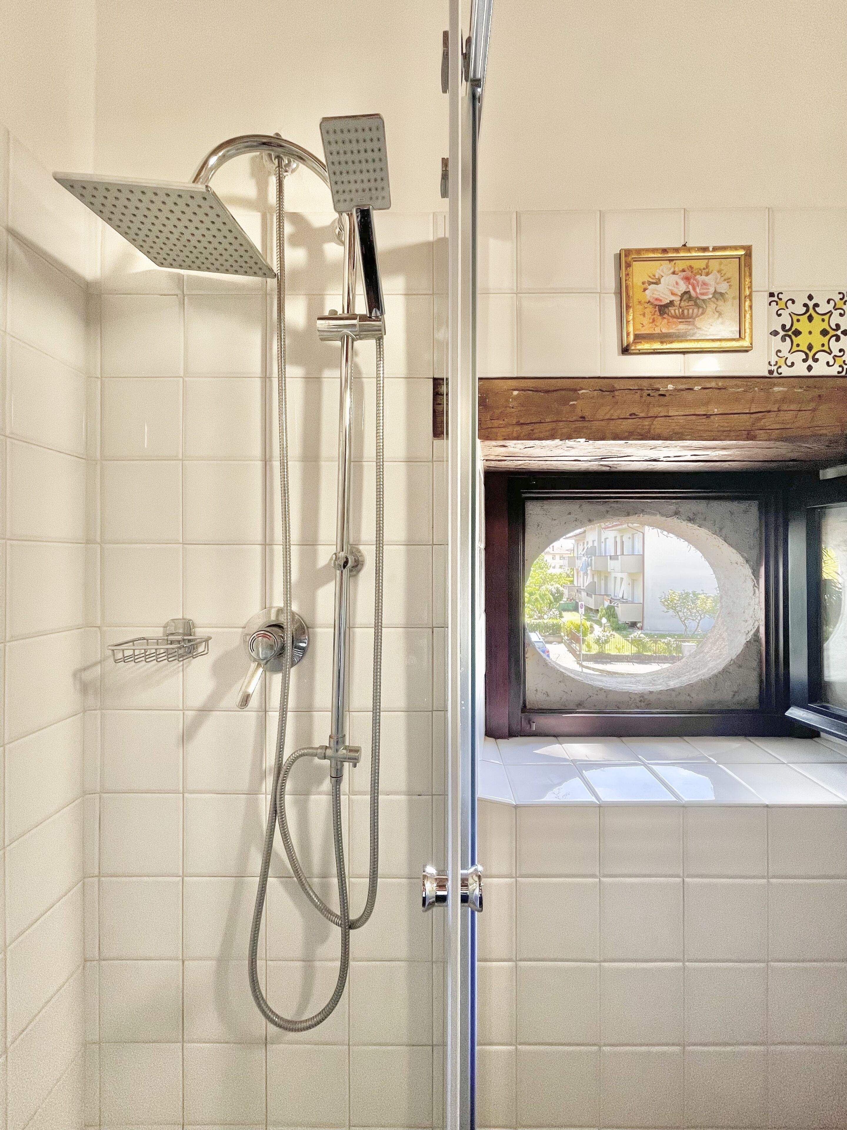 A shower with multiple heads, a glass door, and a view of the outside through a window.