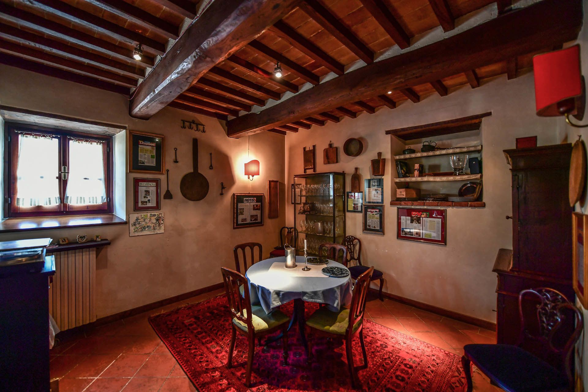 Un comedor con una mesa redonda, sillas, un tapete rojo y una ventana con cortinas.