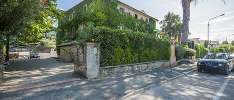 A building with a stone facade, a gated entrance, and a driveway leading to parked cars.