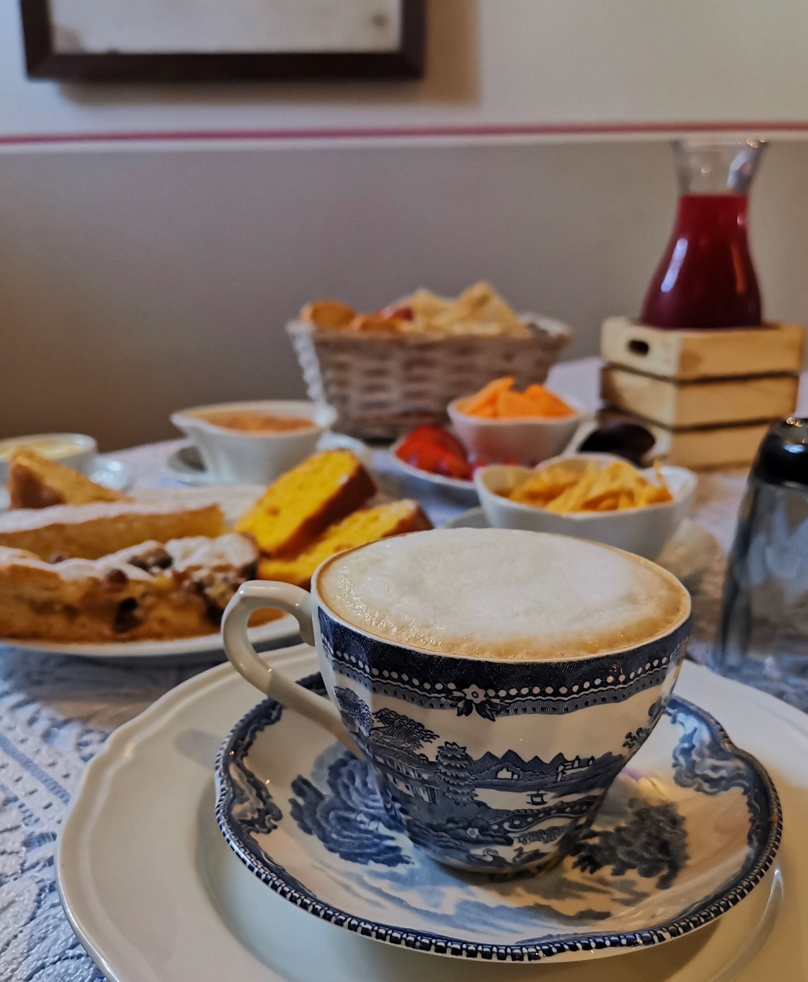 Una tazza di caffè con un piattino decorativo su un tavolo, insieme a diversi pasticcini e ciotole di cibo.