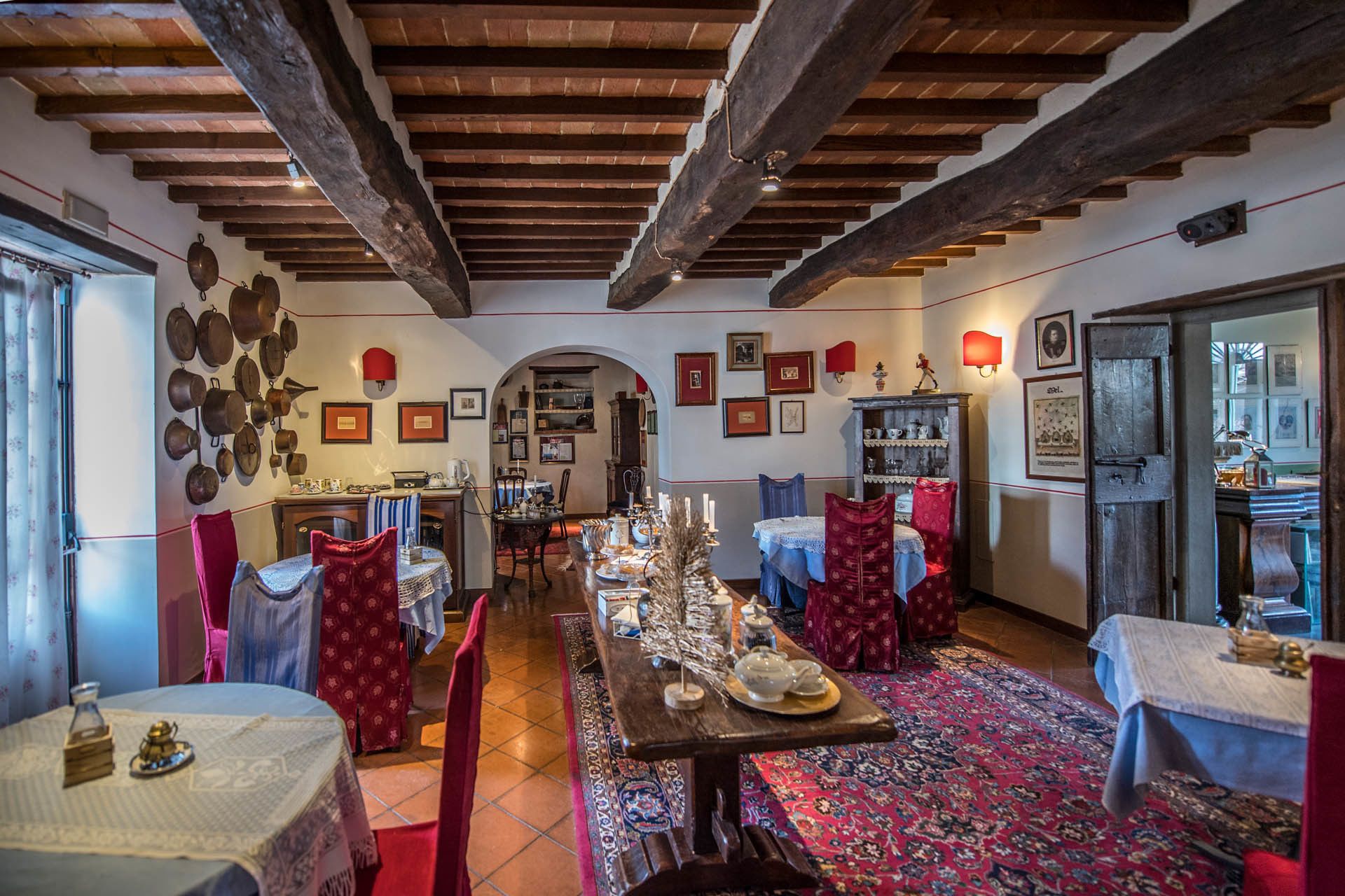 Un comedor tradicional con una larga mesa dispuesta para una comida, vigas de madera en el techo y una alfombra estampada en el suelo.