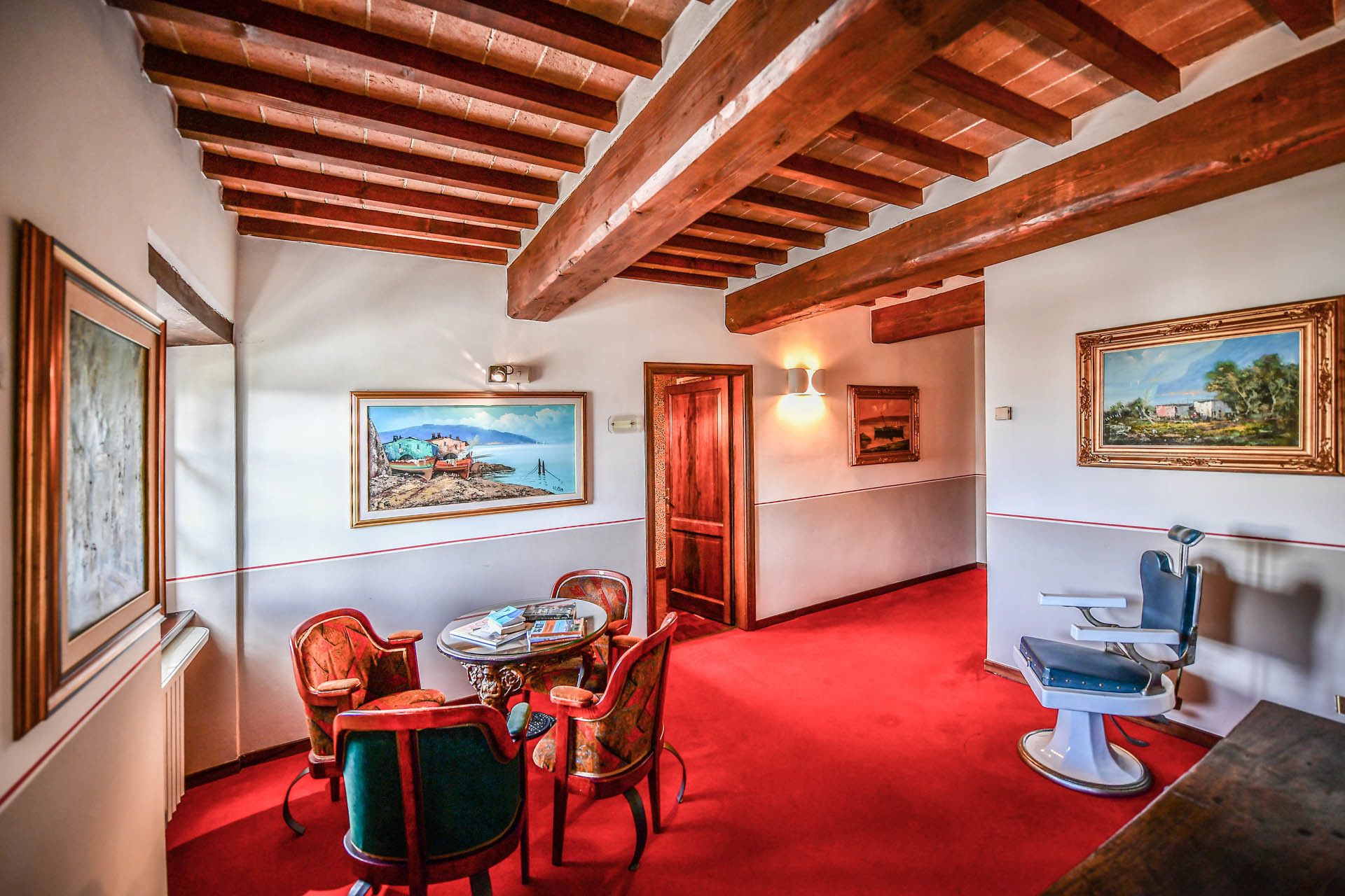 A room with a red carpet, wooden ceiling beams, a dining table with chairs, and a vintage-style bathroom with a blue sink.
