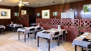 Een restaurant met meerdere tafels, plafondventilatoren en ingelijste foto’s aan de muur.