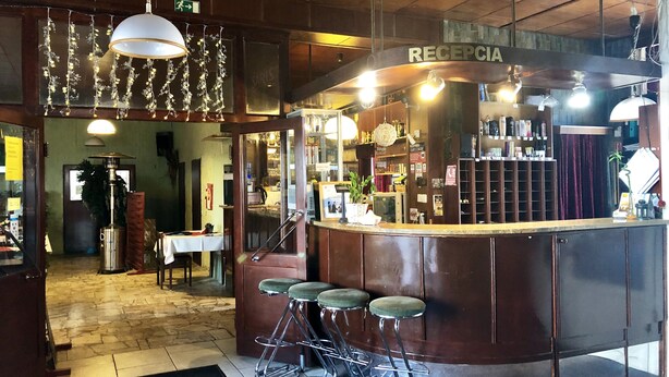 Een bar met een receptiebalie, krukken, hangende lampen en een houten plafond.