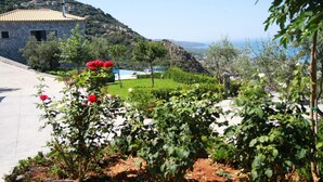 A stone building with a tiled roof, surrounded by lush greenery and a clear view of the sea. - Petra Thea (Kalamata)