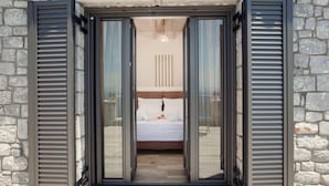 A bedroom with a bed, a nightstand, and a window with blinds. - Petra Thea (Kalamata)