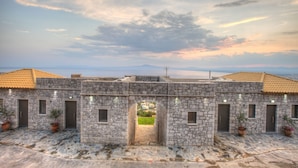 A stone building with a central archway, multiple doors, and potted plants. - Petra Thea (Kalamata)