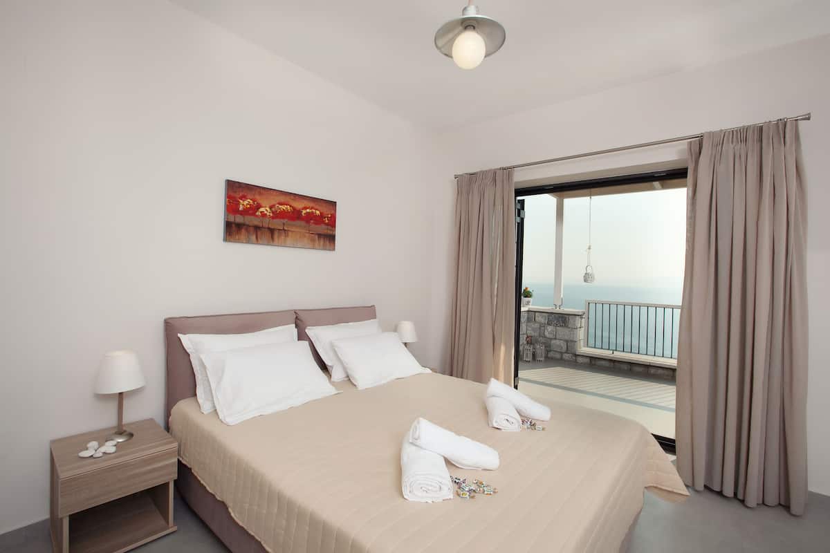 A hotel room with a bed, a nightstand, a painting, and a balcony with curtains.