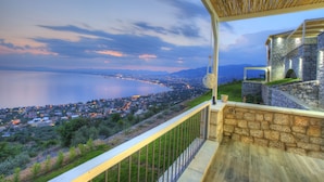 A balcony with a view of a coastal town at dusk, featuring stone architecture and a wooden railing. - Petra Thea (Kalamata)