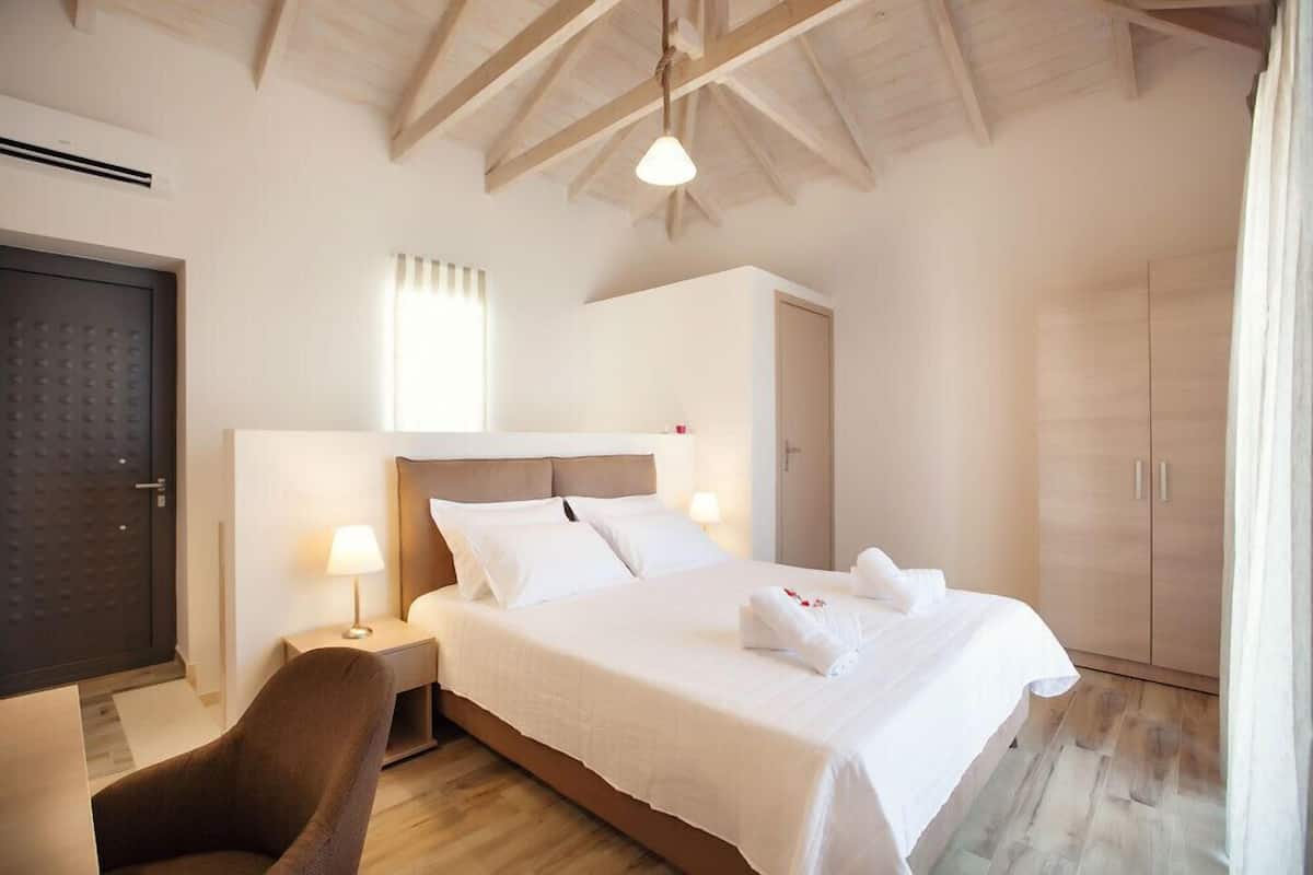 A hotel room with a large bed, a bedside table, a chair, a wardrobe, and a door.