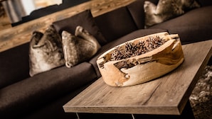 A wooden bowl filled with pinecones on a wooden table in a living room with a dark brown sofa and decorative pillows.