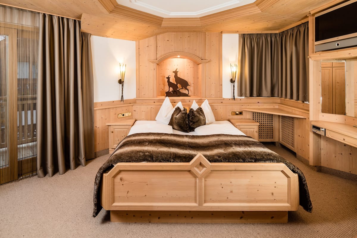 A wooden bedroom with a large bed, a fireplace with a deer silhouette, and a television on a wooden cabinet.