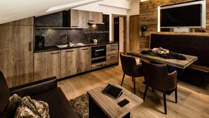 A modern kitchen with wooden cabinets, a dining area with a table and chairs, and a large TV mounted on the wall.