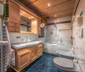 Ein modernes Badezimmer mit Holzschränken, einem großen Spiegel, einer Badewanne und einer Toilette.
