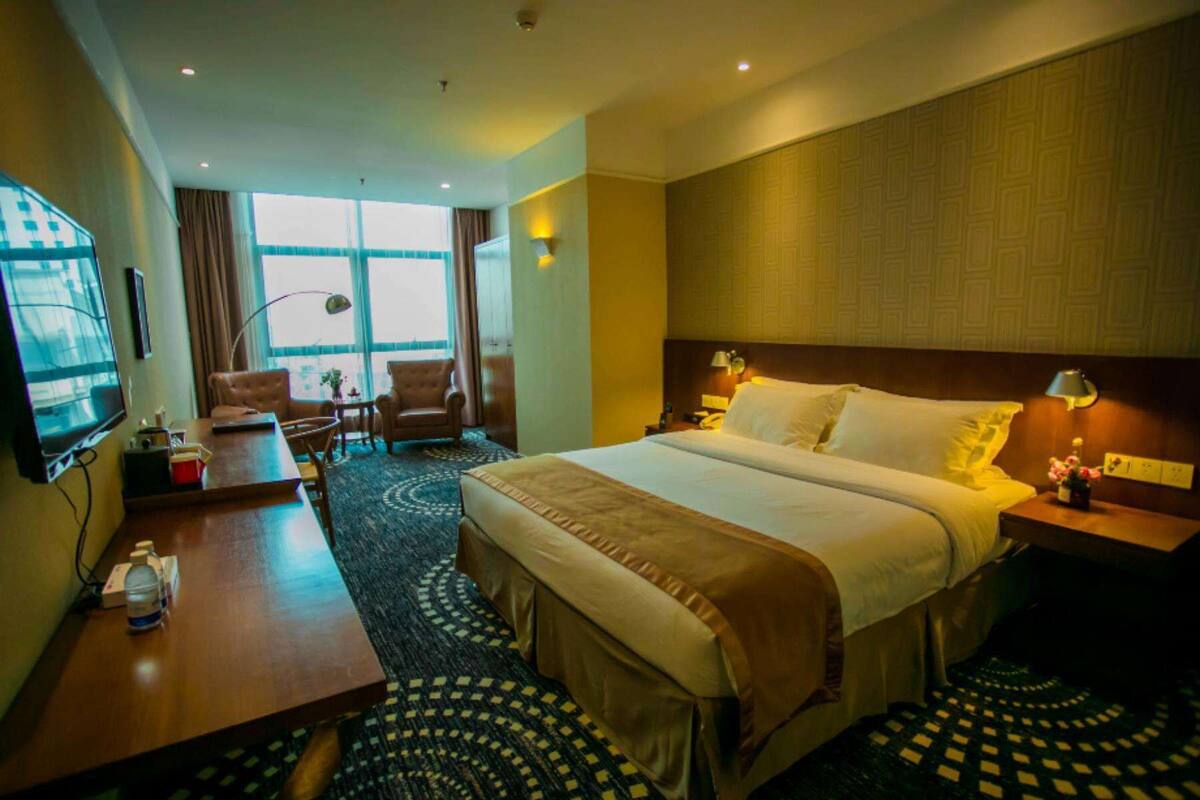 A hotel room with a large bed, a desk, a chair, a TV, and a window with curtains.