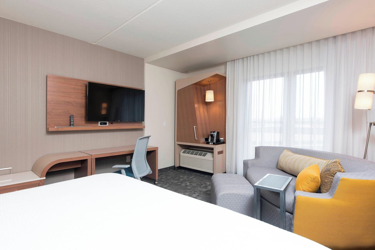 Hotelkamer met een bed, bureau, stoel, bank, televisie, koffiezetapparaat en lamp.