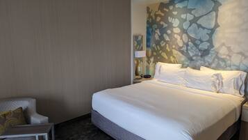 A hotel room with a large bed, a chair, a nightstand, and a wall with a textured pattern.