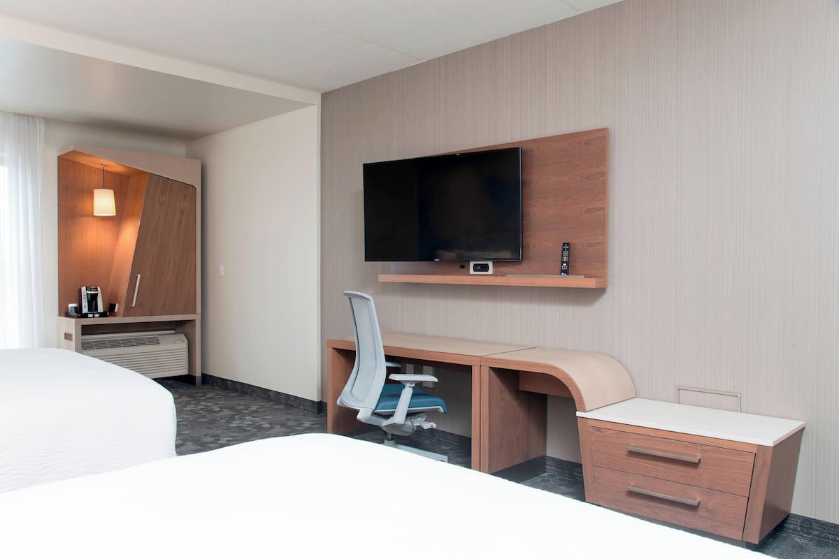 Een hotelkamer met een bed, een bureau met stoel, een televisie en een klein kastje.