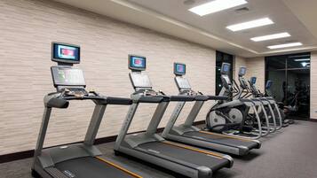 A row of treadmills with digital screens, a control panel, and a mirrored wall.