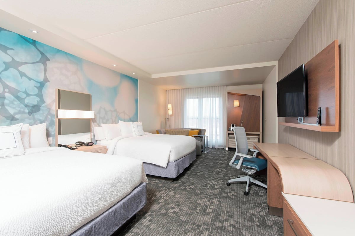 Een hotelkamer met twee bedden, een bureau, een televisie en een badkamer die door een geopende deur zichtbaar is.
