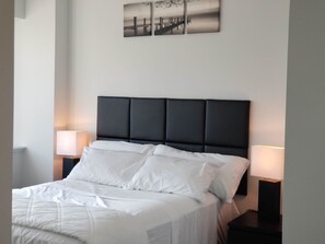 A neatly made bed with white linens, a dark headboard, and two bedside lamps. - Lotus Suites Woodbridge (Iselin)