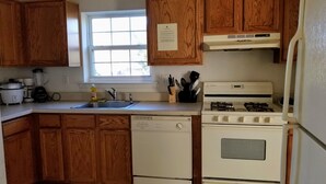 Una cocina con armarios de madera, estufa blanca, lavavajillas y ventana.